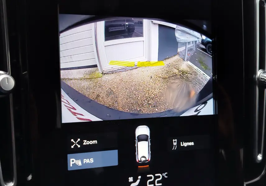 Vue écran caméra de recul du Volvo XC40 beige, montrant l’arrière du véhicule et le sol gravillonné derrière.