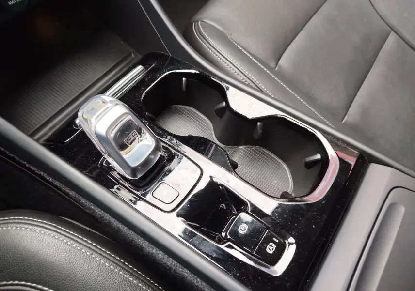 Gros plan sur la console centrale noire avec levier de vitesse cristal et porte-gobelets, siège en cuir noir visible, Volvo XC40.