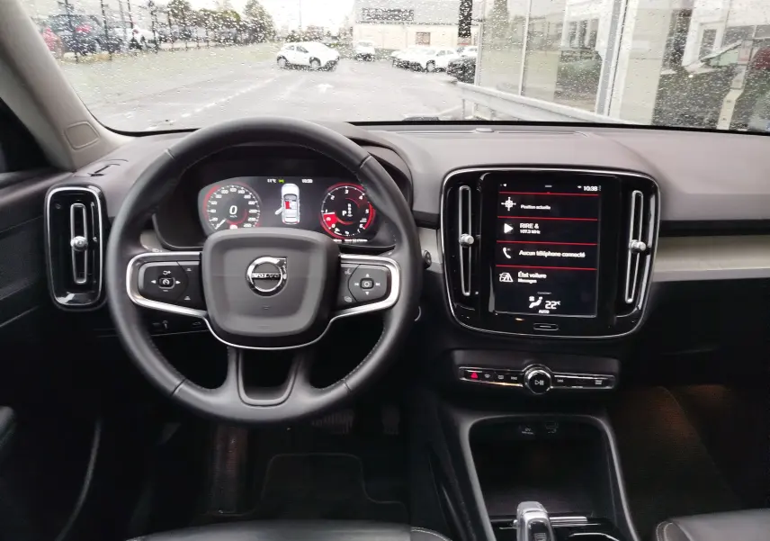 Vue intérieure centrée sur le volant et la console tactile du Volvo XC40 beige, avec tableau de bord numérique allumé.
