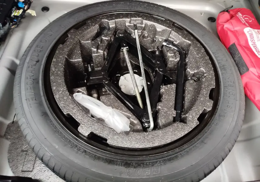Vue rapprochée de la roue de secours et du cric dans le coffre d'un Volvo XC40 beige, version D3 Diesel 2020.