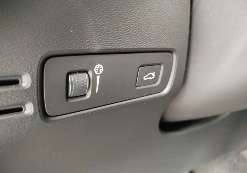 Gros plan sur les commandes intérieures noires du tableau de bord du Volvo XC40 beige, bouton d'ouverture de coffre visible.