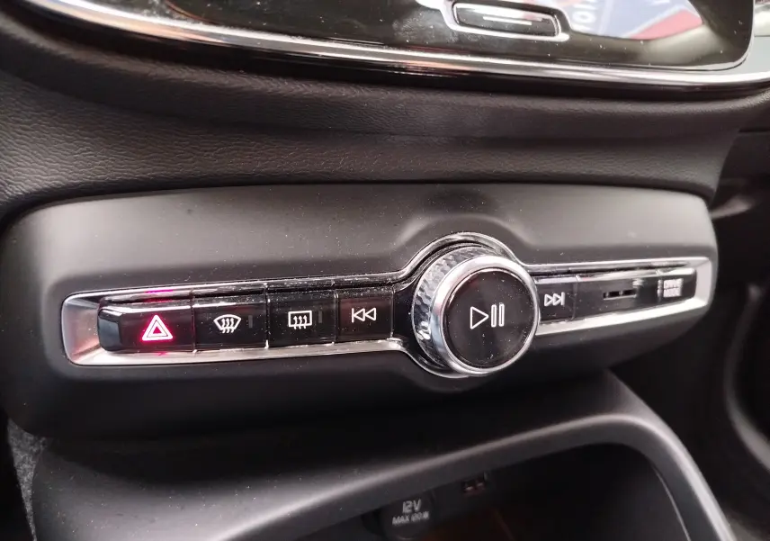 Gros plan sur la console centrale noire du Volvo XC40 beige, avec boutons de commande média et signal d’alerte allumé.
