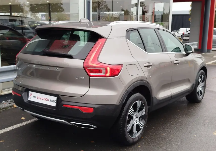 Vue 3/4 arrière droite d'un Volvo XC40 beige 2020 avec feux arrière en forme de C et jantes bi-ton.