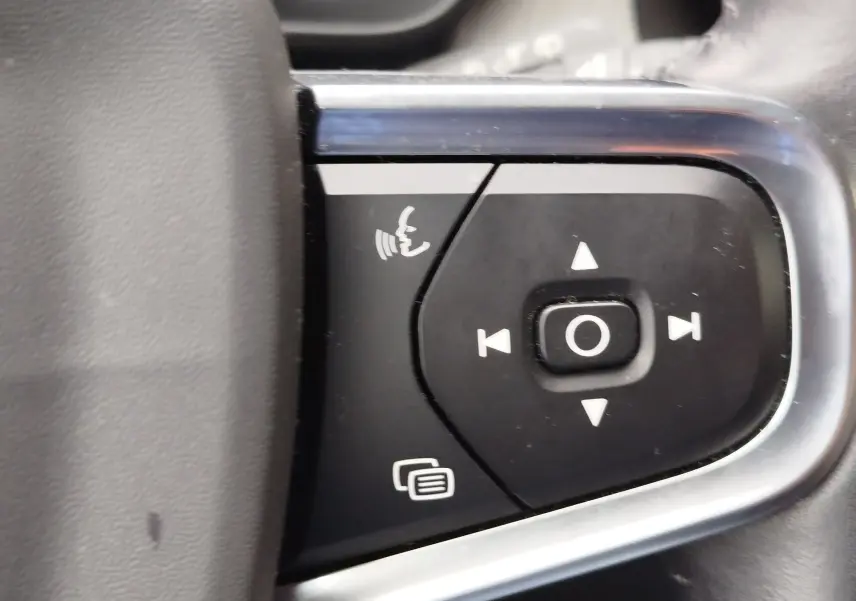 Gros plan sur les commandes noires du volant côté gauche du Volvo XC40 beige, avec boutons de navigation et téléphone.