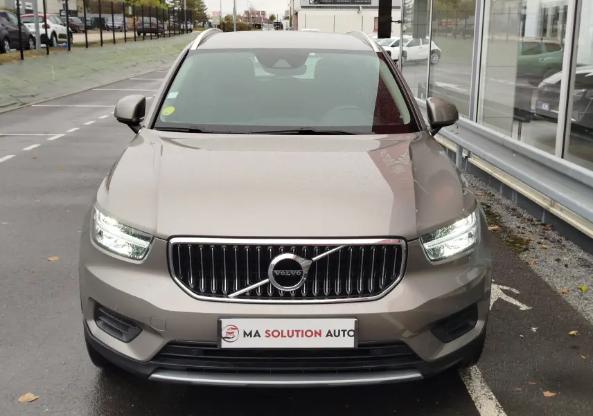 Vue avant d'un Volvo XC40 beige 2020 avec phares LED allumés, calandre chromée et logo central visible.