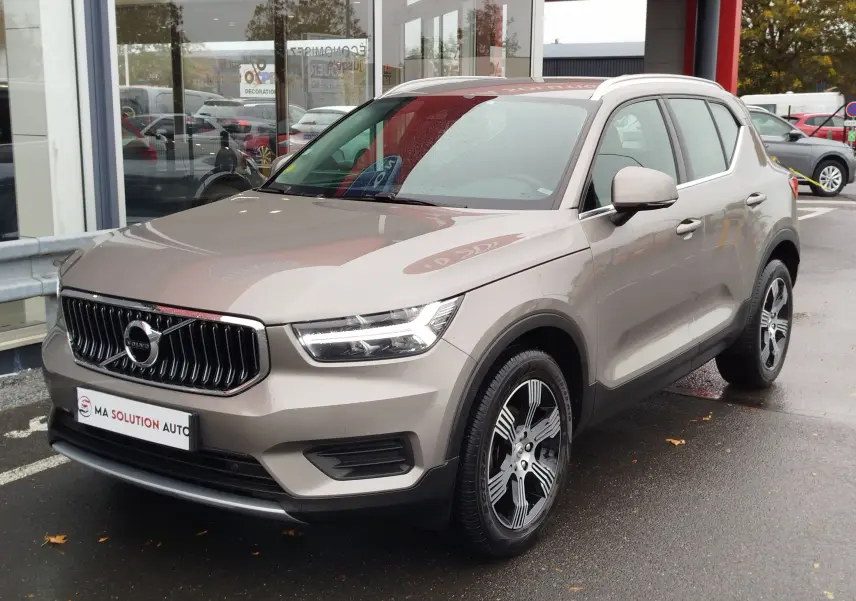 Volvo XC40 beige vue 3/4 avant droit, avec calandre verticale chromée et jantes alliage bicolores.