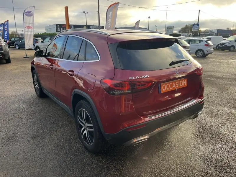 Vue 3/4 arrière droite d'un Mercedes GLA 200 rouge Patagonie métallisé avec vitres arrière surteintées et jantes alliage.