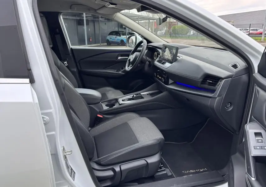 Vue intérieure côté conducteur du Nissan Qashqai blanc nacré 2025, avec tableau de bord moderne et éclairage d'ambiance bleu.