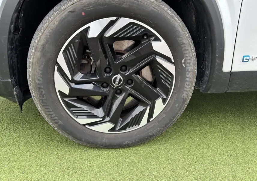 Gros plan sur la roue avant gauche du Nissan Qashqai blanc nacré, avec jante alliage noire et argentée au design moderne.