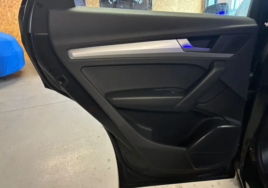 Vue intérieure de la porte arrière gauche noire de l'Audi Q5 2024 avec insert argenté et commandes intégrées.