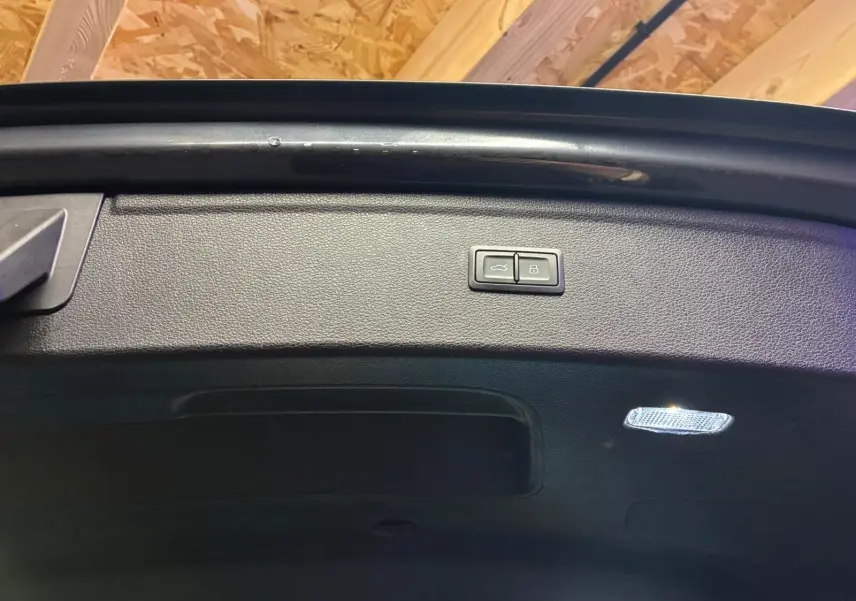Bouton d'ouverture et de verrouillage sur le hayon intérieur noir du coffre d'un Audi Q5 gris 2024.