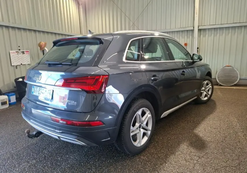 Audi Q5 gris hybride rechargeable vu en 3/4 avant droit dans un garage avec jantes 5 branches doubles.