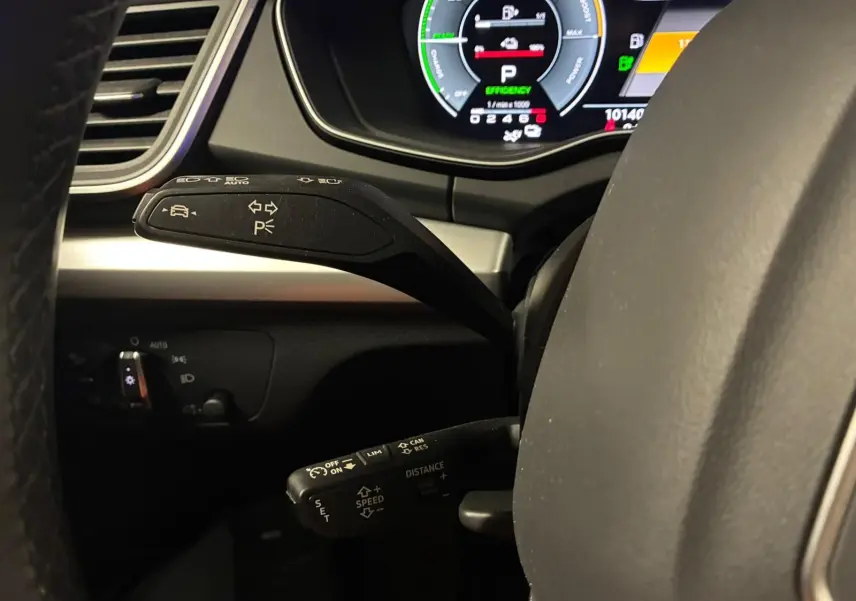 Gros plan sur les commandes au volant côté gauche de l'Audi Q5 gris, avec tableau de bord numérique en arrière-plan.