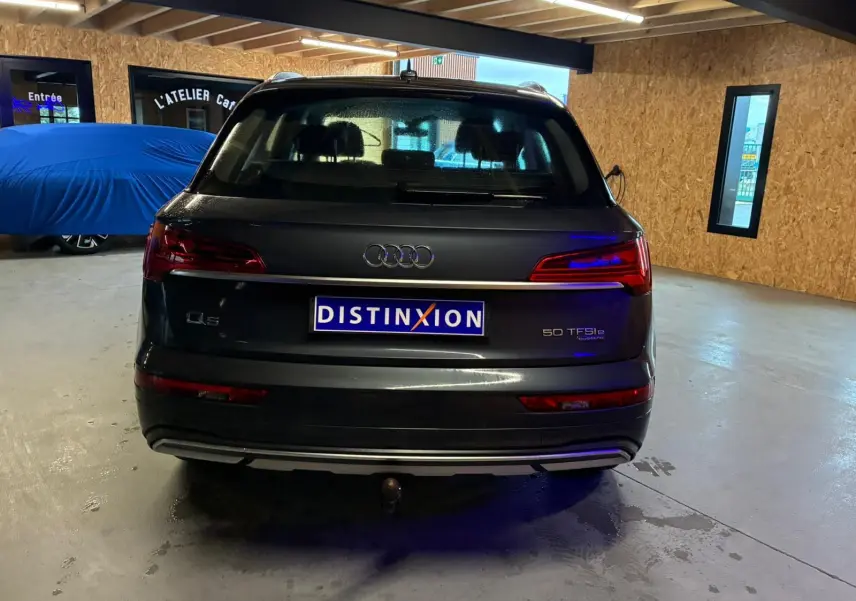 Vue arrière d'un Audi Q5 gris 2024 hybride rechargeable avec attelage visible en intérieur d'atelier.