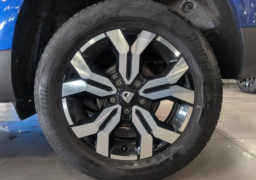 Gros plan sur la roue avant droite du Dacia Duster Bleu Iron 2022, mettant en valeur la jante alliage bicolore et le pneu Bridgestone.