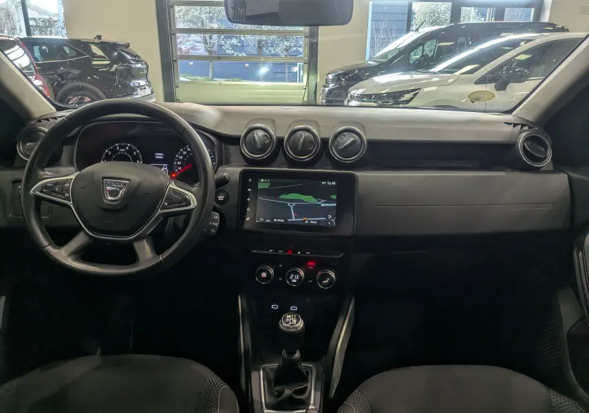 Vue intérieure frontale du tableau de bord noir du Dacia Duster 2022 avec volant multifonction et écran tactile central.