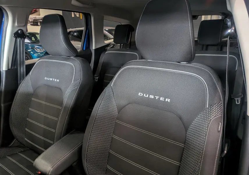 Gros plan sur les sièges avant noirs en tissu du Dacia Duster 2022 avec logo DUSTER brodé, intérieur visible en arrière-plan.