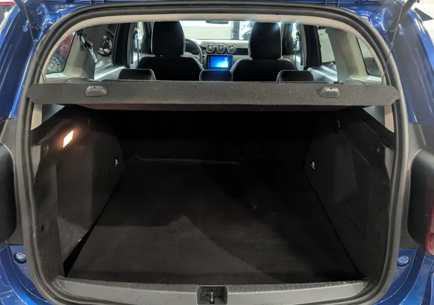 Coffre ouvert d’un Dacia Duster bleu Iron 2022, vue arrière avec intérieur noir et tablette de séparation.