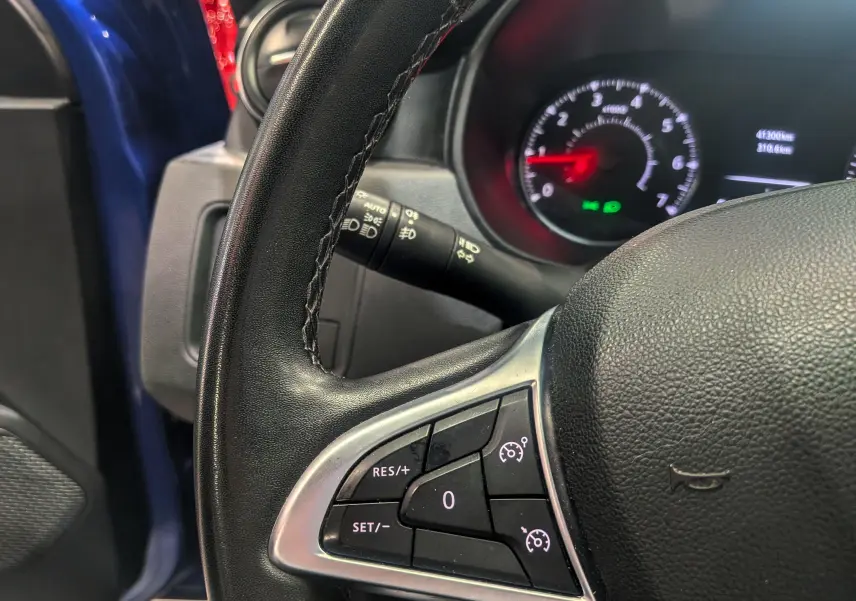 Gros plan sur le volant côté gauche du Dacia Duster bleu Iron, avec commandes de régulateur de vitesse et tableau de bord en arrière-plan.