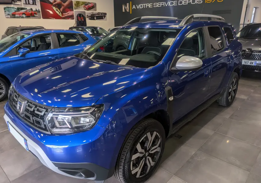 Vue 3/4 avant droite du Dacia Duster 2022 bleu Iron avec rétroviseurs argentés et jantes bi-ton en concession.