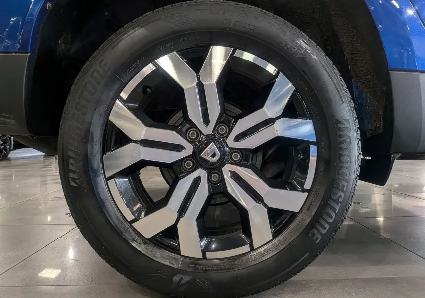 Gros plan sur la jante alliage bicolore du Dacia Duster Bleu Iron, mettant en valeur le logo central et le pneu Bridgestone.