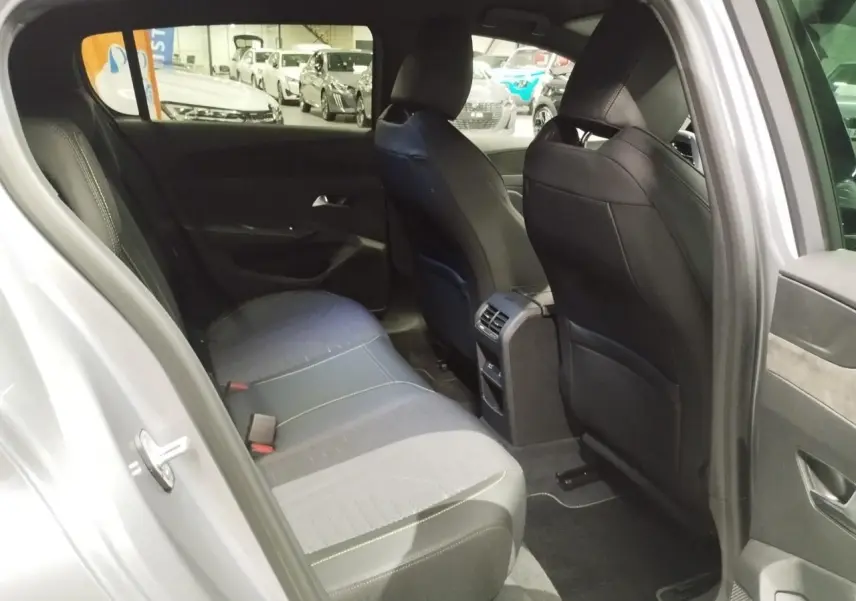 Vue intérieure arrière côté gauche d'une Peugeot 308 gris Artense, montrant la banquette et les sièges avant en tissu noir avec surpiqûres.