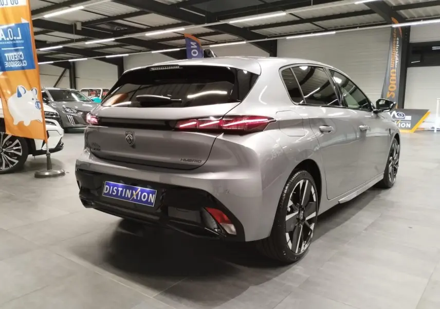 Vue 3/4 arrière droite d'une Peugeot 308 hybride gris Artense avec feux arrière LED en forme de griffes et jantes alliage 18 pouces.