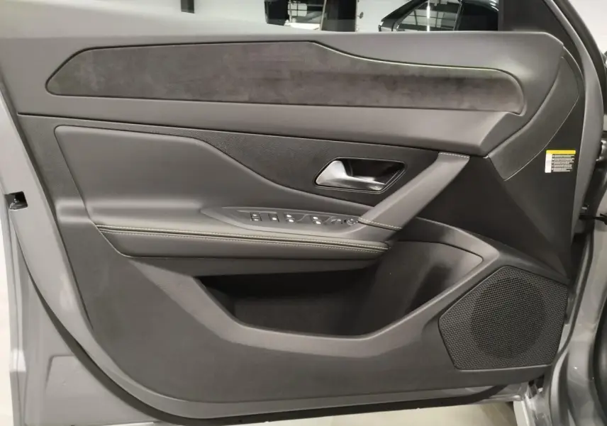 Vue rapprochée de la porte avant gauche gris Artense de la Peugeot 308 Hybrid avec surpiqûres vert Adamite et haut-parleur intégré.