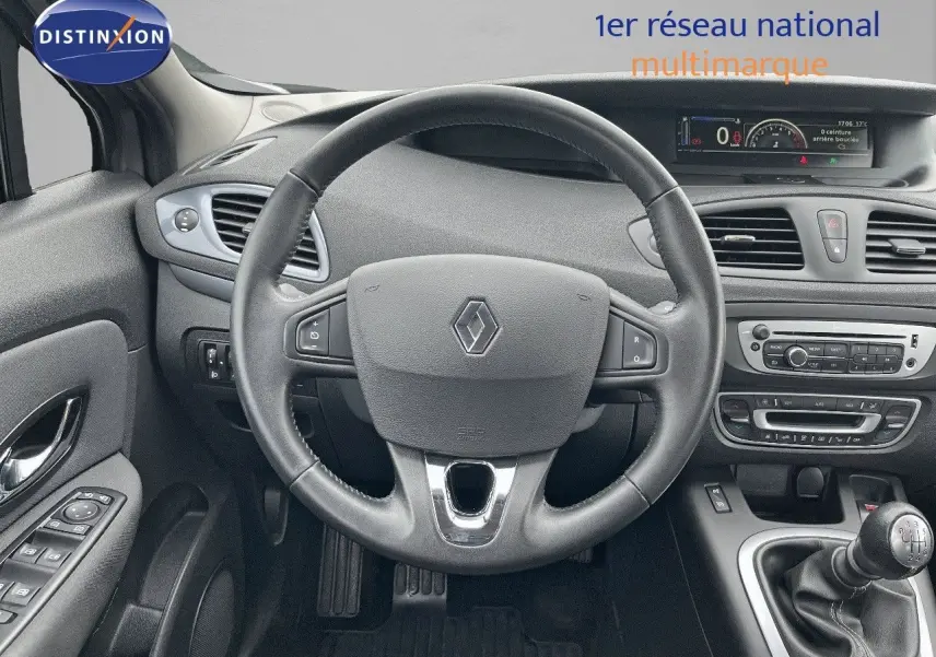 Vue intérieure frontale du tableau de bord gris du Renault Scénic III 2015 avec volant et levier de vitesse manuel.