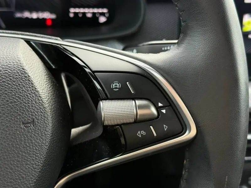 Gros plan sur les commandes du volant du Skoda Kamiq 2024, avec molette métallique et boutons noirs encadrés de chrome.