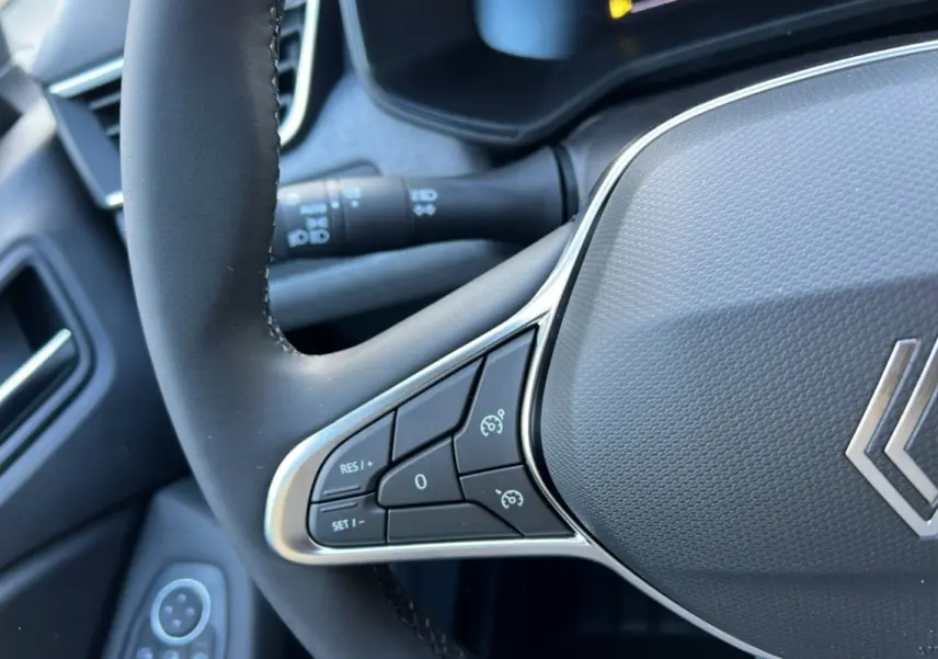 Gros plan sur le volant multifonctions gris et noir de la Renault Clio 2025, avec commandes de régulateur de vitesse.