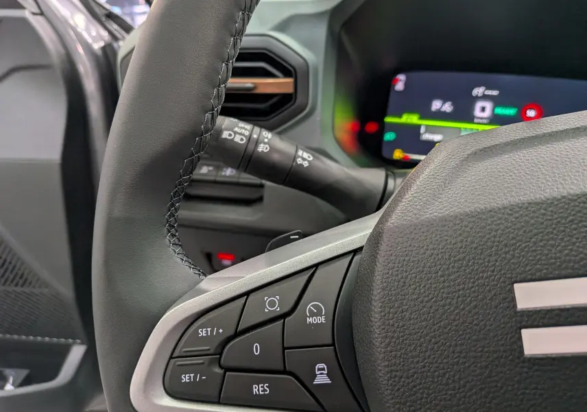 Gros plan sur le volant noir avec commandes multifonctions du DACIA BIGSTER Hybrid-G 150 4x4, tableau de bord numérique en arrière-plan.