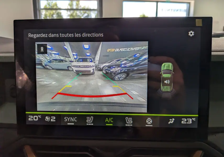 Vue caméra de recul montrant un Dacia Bigster gris schiste en intérieur, avec lignes de guidage colorées à l’écran.