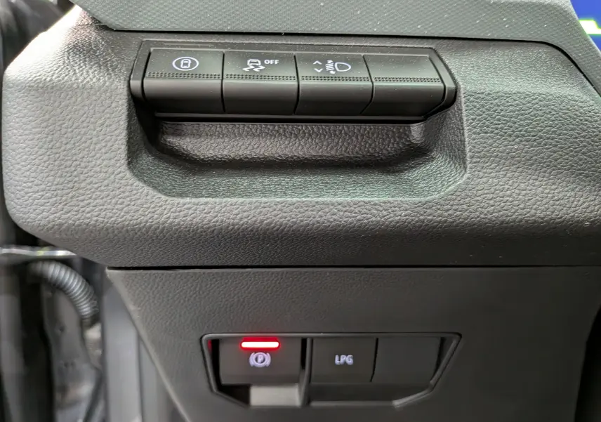 Gros plan sur les commandes du tableau de bord du Dacia Bigster Hybrid-G 150 4x4, avec bouton frein à main électronique allumé.