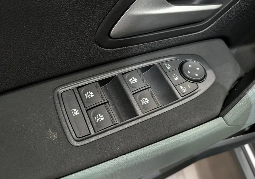 Gros plan sur les commandes de lève-vitres et rétroviseurs côté conducteur du Dacia Bigster Hybrid-G 150 4x4 gris Schiste.