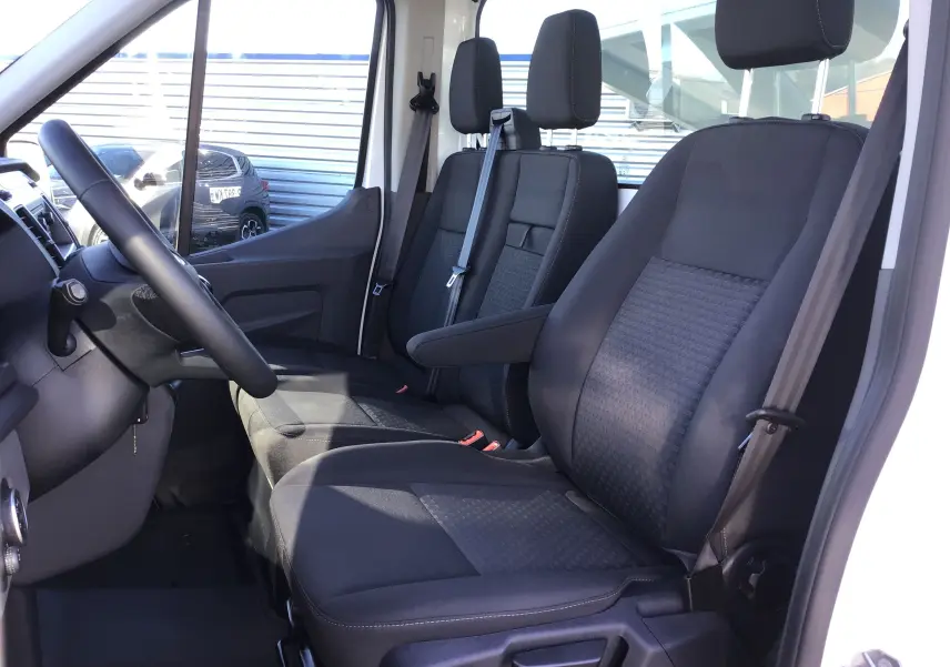 Vue intérieure côté conducteur du Ford Transit Chassis Cabine blanc 2024 avec sièges noirs et volant multifonction.