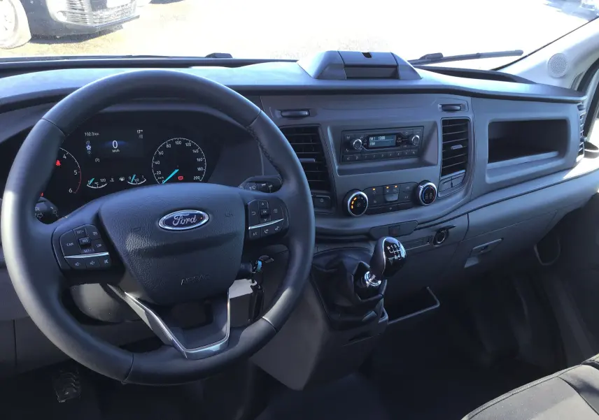 Vue intérieure du tableau de bord et volant du Ford Transit Chassis Cabine blanc, avec levier de vitesses manuel visible.