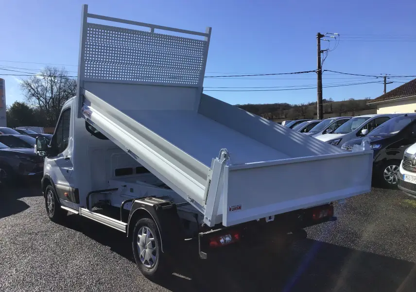 Ford Transit Chassis Cabine blanc vu en 3/4 arrière droit avec benne basculante relevée sur parking ensoleillé.