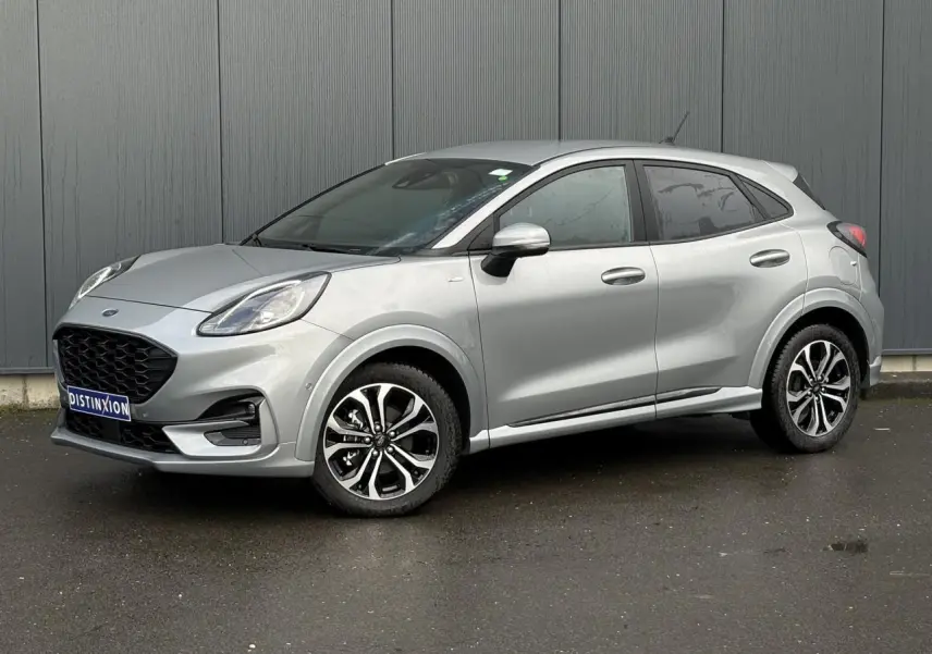 Vue 3/4 avant droit d'un Ford Puma gris Solar avec jantes alliage et vitres surteintées, garé devant un mur gris.