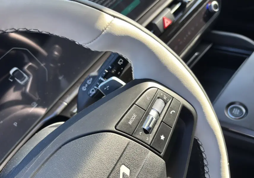 Gros plan sur le volant cuir clair du KIA SPORTAGE 2026, avec commandes multifonctions et tableau de bord numérique en arrière-plan.