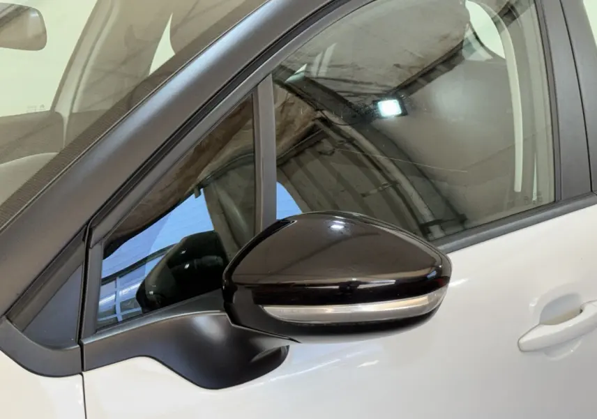 Gros plan sur le rétroviseur noir côté conducteur d'une Citroën C3 blanche vue de profil gauche.