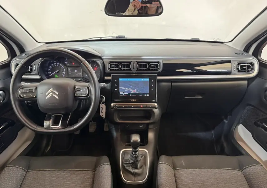 Vue intérieure avant du tableau de bord noir et volant cuir de la Citroën C3 blanche avec écran tactile central et boîte manuelle.