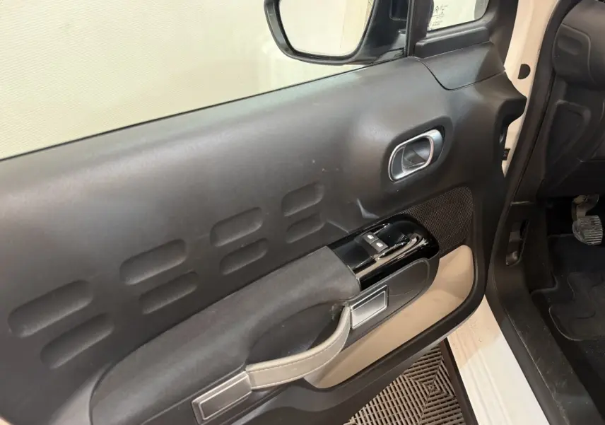 Vue intérieure du panneau de porte côté conducteur d'une Citroën C3 blanche, avec commandes de vitres et poignée intégrée.