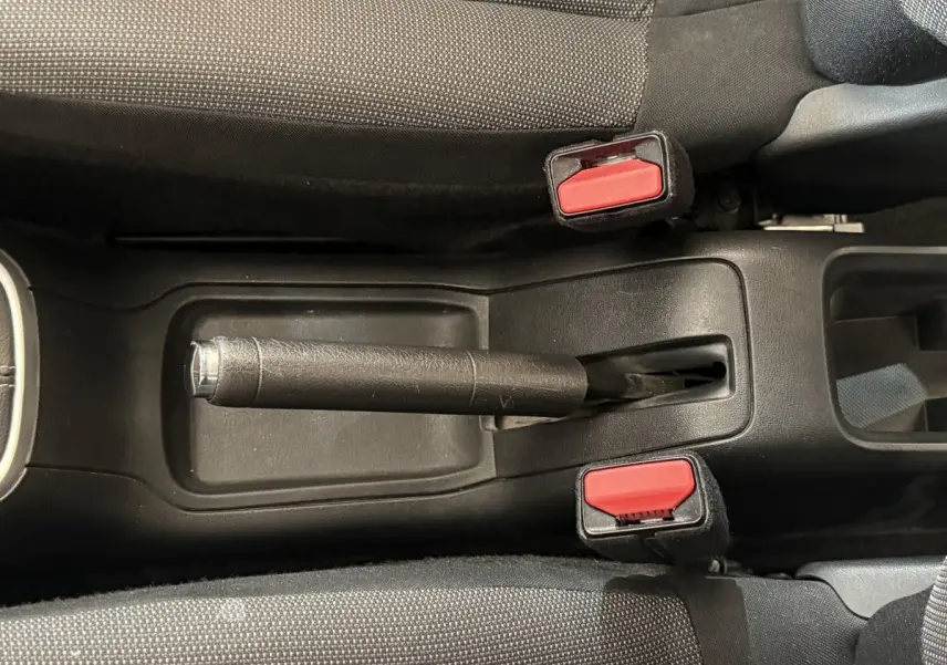Vue plongeante sur le frein à main noir et les ceintures de sécurité rouges de la Citroën C3 blanche, intérieur tissu gris.