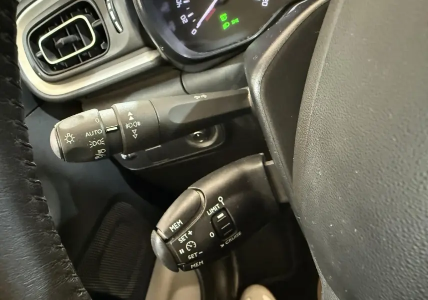 Gros plan sur la commande de régulateur de vitesse et les commandes d’éclairage côté gauche du tableau de bord noir d’une Citroën C3 blanche.