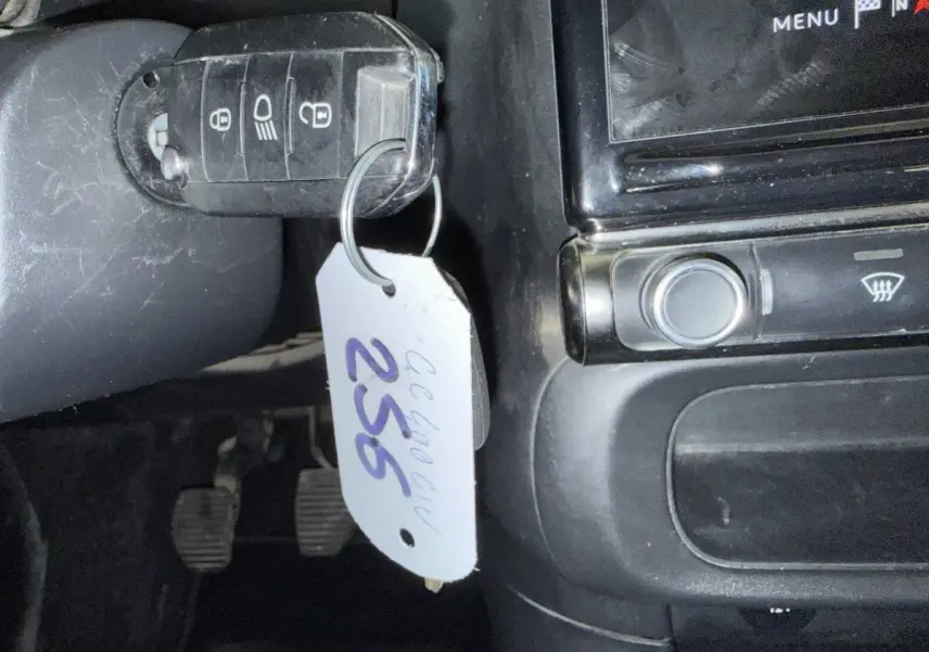 Gros plan sur la clé de contact avec étiquette suspendue dans l'habitacle noir d'une Citroën C3 blanche.