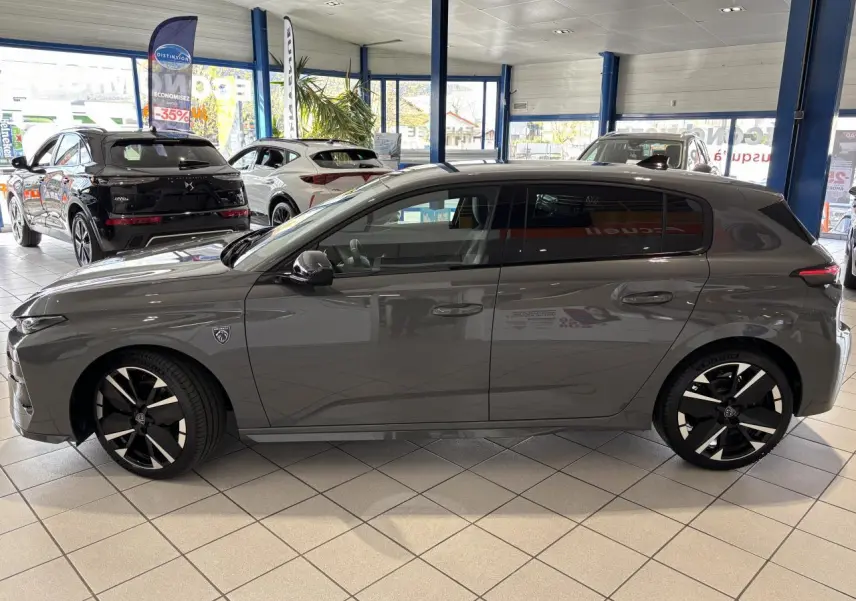 Vue de profil côté gauche d’une Peugeot 308 gris selenium en showroom avec jantes alliage noires et blason sur aile avant.