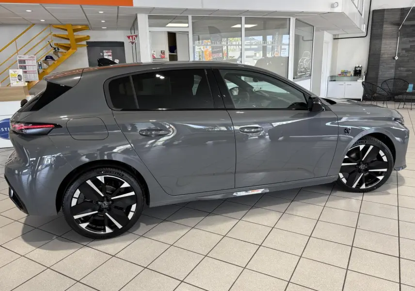 Peugeot 308 gris sélénium vue de profil côté gauche en intérieur avec jantes alliage bicolores et vitres teintées.