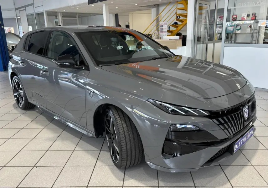 Peugeot 308 gris selenium vue 3/4 avant droit en showroom avec calandre noire et jantes alliage bi-ton.