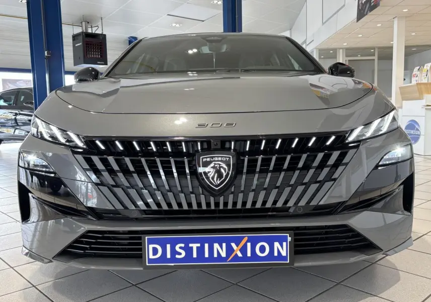 Vue avant d'une Peugeot 308 gris selenium avec calandre noire brillante et logo lion illuminé en concession.